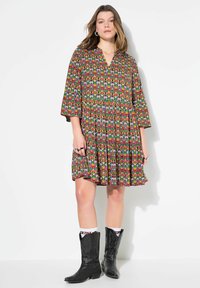 Kleid mit kurzen Ärmeln, buntem geometrischem Muster, V-Ausschnitt und gestuftem Rock, kombiniert mit schwarzen Cowboy-Stiefeln und weißen Socken.
