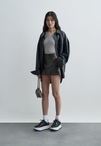 Must ülekaalukas särk, hall soonikkoes topp, pruun nahast seelik nähtavate õmblustega, mustad platvorm-tossud ja väike hall käekott.