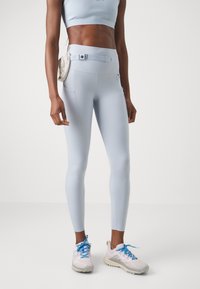 Világoskék leggings oldalsó zsebekkel és állítható derékkal, fehér sportcipővel, kék fűzőkkel párosítva.