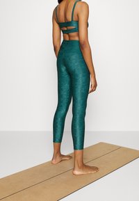 Teal träningsset bestående av en kort topp med utskärning och högmidjade tights, båda tillverkade av textil med stretch.