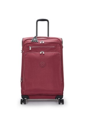 Red fabric suitcase with two zippers, black wheels, and a retractable handle. Features a circular logo and a decorative bear keychain.