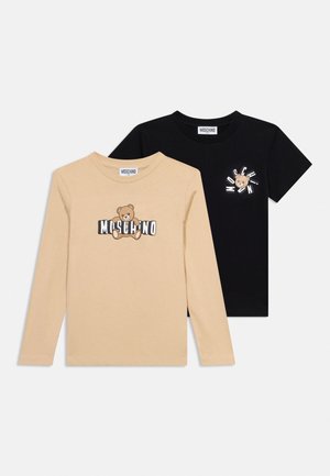 T-shirts Moschino beige à manches longues et noirs à manches courtes avec logo ours en peluche et nom de la marque sur le devant, fond blanc.