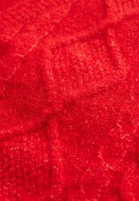 Tessuto a maglia rosso con un motivo testurizzato, che mostra una consistenza morbida e pelosa e un colore caldo e vibrante in tutto.