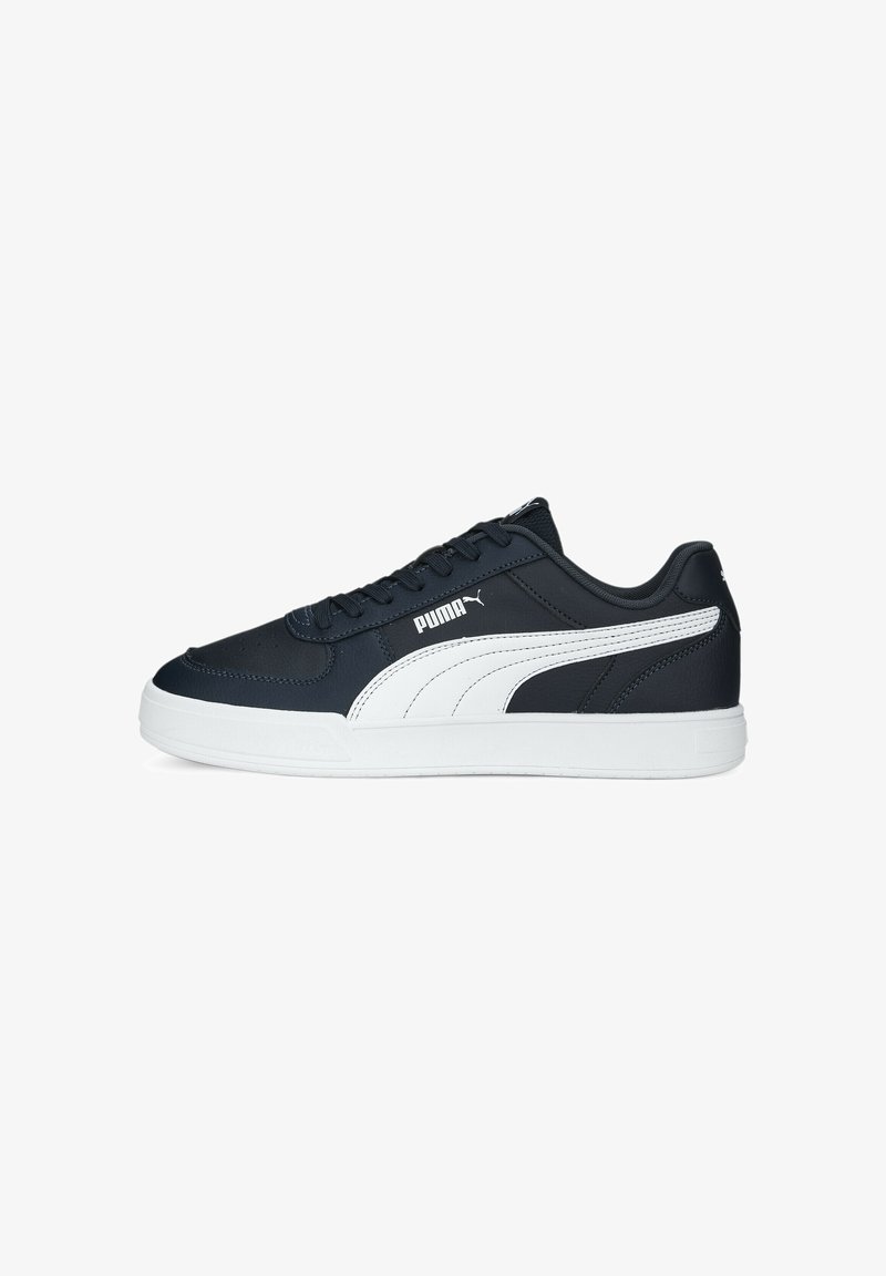 Baskets Puma noires basses avec une bande blanche sur le côté, une semelle blanche et des lacets noirs, présentées de profil face à gauche.