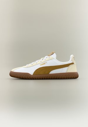 Baskets Puma blanches et marron avec semelle en gomme, bande latérale en daim, fermeture à lacets à l'avant, et logo sur le côté et la languette sur fond neutre.
