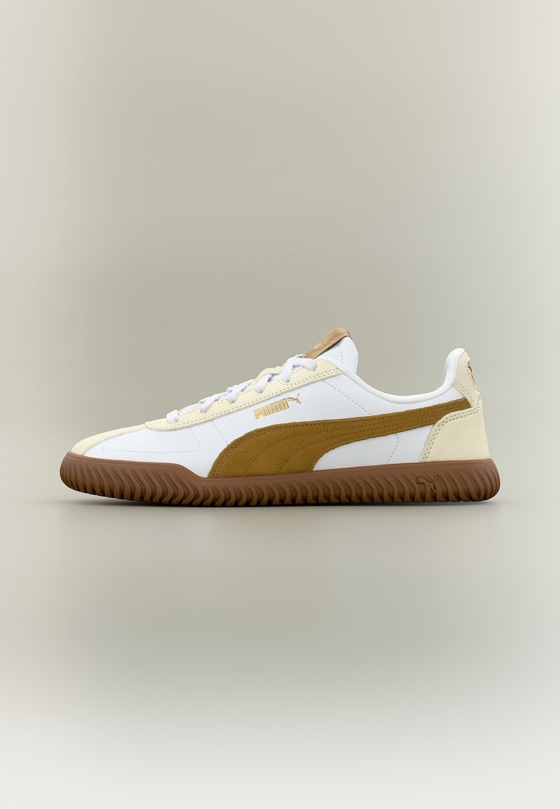 Baskets Puma blanches et marron avec semelle en gomme, bande latérale en daim, fermeture à lacets à l'avant, et logo sur le côté et la languette sur fond neutre.