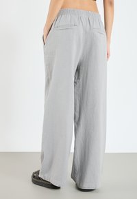 Pantalons larges gris clair avec une taille élastique, dotés de deux poches arrière et d'une texture douce. Idéal pour une tenue décontractée.