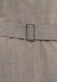 Opásaný oděv vyrobený z texturované šedé tkaniny s jemnými modrými a oranžovými skvrnami. Obsahuje obdélníkovou kovovou sponu a hladký povrch.