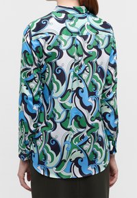 Chemise à manches longues avec un motif tourbillonnant multicolore vert, bleu et noir. Fabriquée dans un tissu lisse, elle possède un col à revers et des poignets boutonnés.