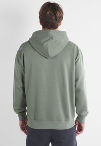 Sweat à capuche vert en tissu doux, avec une grande capuche à l'arrière, des poignets côtelés et un ourlet droit. Petit logo sur une épaule.