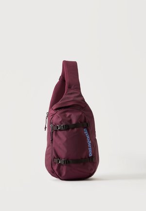 Jednoramienny plecak na ramię w kolorze bordo z dwoma czarnymi paskami z klamrami i niebieskim logo "Patagonia" na przedniej kieszeni.
