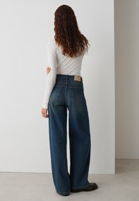High-waisted wide-leg blue denim jeans with back pockets and a tan label. The fabric has a sturdy texture with a slight fade.