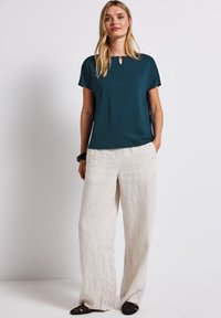 Tee groen kortmouw top met een keyhole halslijn, gecombineerd met losse, lichtbeige linnen broeken. Geen patronen zichtbaar, gladde textuur.