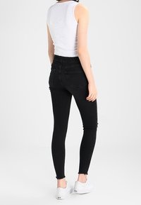 Svarta smala jeans med fransad nederkant, med klassisk femfickdesign. Kombinerat med en åtsittande vit linne och vita sneakers.