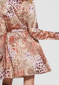 Robe à manches longues avec une jupe fluide, présentant un mélange d'imprimés cachemire et animalier dans des tons chauds de beige, orange, violet et rouge.