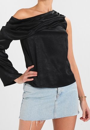 Kvinde iført en sort asymmetrisk off-shoulder top med et langt ærme og en lyseblå denim mini nederdel.