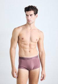 Moške hlačke Calvin Klein v mauve barvi, z gladkim materialom, elastičnim pasom z logotipom in prileganjem, ki poudarja obliko telesa.
