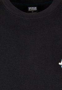 Camiseta de algodón negra con cuello redondo y un pequeño gráfico multicolor de una nube en el lado derecho. Etiqueta visible en el interior.