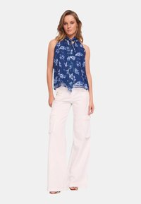 Top senza maniche blu a fiori con scollo annodato, abbinato a pantaloni cargo bianchi a gamba larga con tasche laterali e dettagli hardware sottili.