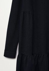 Vêtement noir à manches longues avec des détails de tissu froncé à la taille et à l'ourlet, et de larges poignets aux manches.