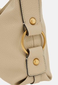 Borsa a mano in pelle beige con superficie tessurizzata, hardware dorato e un accento a forma di anello. Dettagli cuciti lungo i contorni.