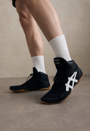 Juodi aukšti sportiniai bateliai turi tekstūruotą audinio viršutinę dalį, baltus logotipo akcentus ir guminius padus. Dėvimi su baltais kulkšnies šortais.