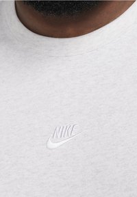 Grå bomullströja med rund hals och en vit broderad Nike-logotyp på bröstet. Mjuk tyg med en texturerad yta.