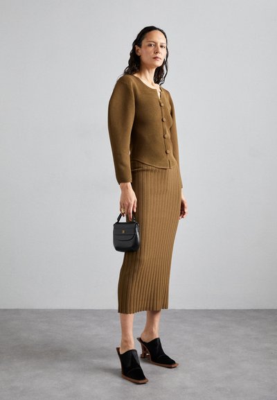 Bruine geribde gebreide cardigan met knoopsluiting en bijpassende geribde rok. Zwarte muiltjes en een kleine zwarte handtas maken de outfit compleet.