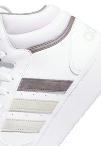 Scarpa sportiva bianca con dettagli in pelle texturizzata e scamosciata, in strisce grigie chiare e beige. Punta arrotondata e collare imbottito.