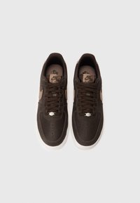 Par tenisica Nike Air Force 1 tamnosmeđe boje s bež swoosh logotipima i bijelim potplatima pregledane odozgo na bijeloj pozadini.