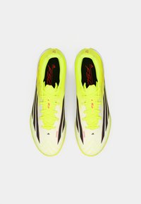 Λαμπερά κίτρινα ποδοσφαιρικά παπούτσια με μαύρες ρίγες, με υφή επιφάνειας και σχέδιο που δένει με κορδόνια. Ο σχεδιασμός του μοντέλου "F50" είναι ορατός.