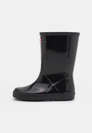 Bota de lluvia de goma negra brillante con suela texturizada y una pequeña etiqueta rectangular cerca de la parte superior frontal, sobre un fondo blanco.