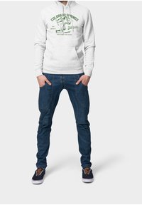 Felpa grigia con grafica verde recante la scritta "COLORADO SPRINGS" e jeans blu con taglio e cuciture uniche, abbinati a sneaker scure.