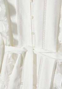 Robe en lin blanc avec fermeture à boutons sur le devant, accents en dentelle et ceinture nouée à la taille. Comprend des volants et un tissu texturé pour plus de détails.