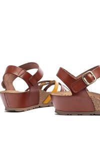 Sandali wedge in pelle marrone con soletta in sughero, cinturini regolabili alla caviglia e un accento giallo su una scarpa. Suola texture per la presa.