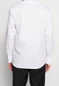 Biała koszula z długim rękawem wykonana z gładkiej tkaniny, z klasycznym kołnierzykiem i mankietami na guziki, pokazana od tyłu z zaokrąglonym dołem.