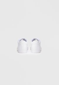 Ein Paar weiße Low-Top-Sneaker von hinten betrachtet, mit Zugschlaufen und dezentem Logo auf weißem Hintergrund.