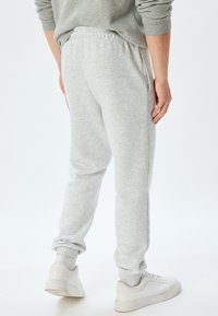 Grå sweatpants med elastisk talje og manchetter, der har sidelommer og et blødt, struktureret stof. Båret med hvide sneakers.