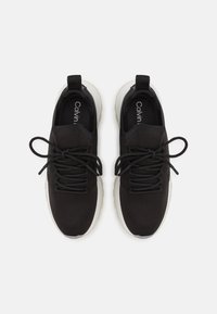 Scarpe sportive nere con tomaia texturizzata, lacci rotondi e suola bianca. Presentano un logo sulla soletta e un tab di trazione rinforzato sul tallone.