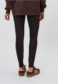 Dunkelbraune Leggings mit einem schwarzen Leopardenmuster, die einen enganliegenden Schnitt haben, kombiniert mit braunen Sneakern mit pinken Akzenten.