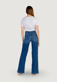High-waisted, wide-leg denim jeans in dark blue with faded accents, featuring back pockets and a classic button closure. Paired with a white t-shirt.
