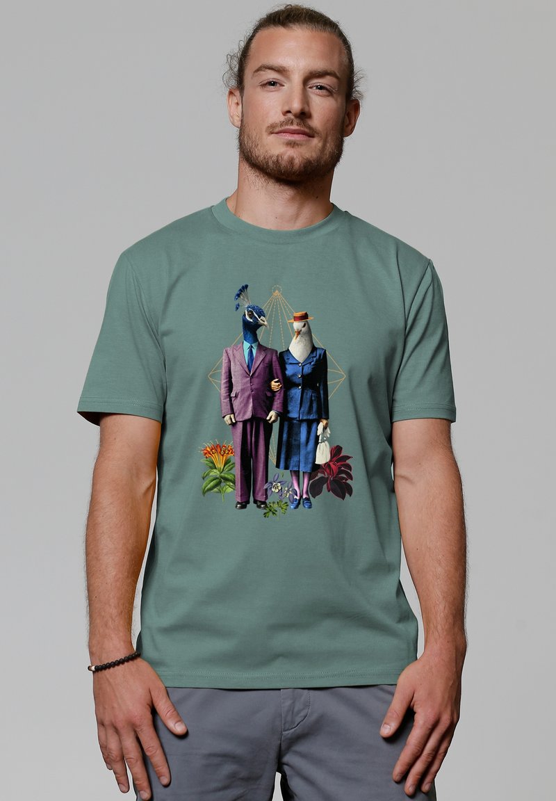 Grafische t-shirt met een illustratie van twee vogels in formele kleding, tegen een groene achtergrond met bloemaccenten.