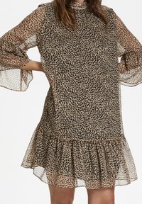 Djurtrycksklänning i lätt, genomskinlig tyg med en volangkant. Har långa ärmar med utsvängda manschetter, som blandar beige och svarta nyanser.