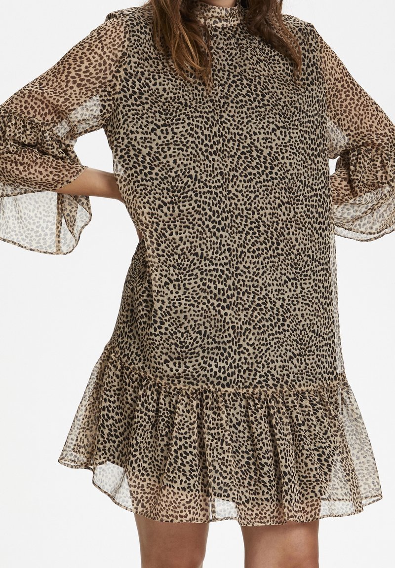 Djurtrycksklänning i lätt, genomskinlig tyg med en volangkant. Har långa ärmar med utsvängda manschetter, som blandar beige och svarta nyanser.