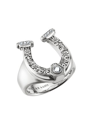 Anello d’argento a forma di ferro di cavallo con incisioni floreali, piccoli cristalli incastonati e una pietra centrale trasparente.