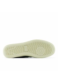 Vihreän tennarin pohja, jossa on kuvioitu kumipohja siksak-kuviolla ja kantapään lähellä oleva pyöreä logoyksityiskohta, jota ympäröi kermaan vivahtava reuna.