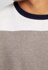 Kurzarm-Pullover mit einem gerippten kragen in Marineblau; zeigt horizontale Streifen in hellgrauem und beigem strukturiertem Stoff.