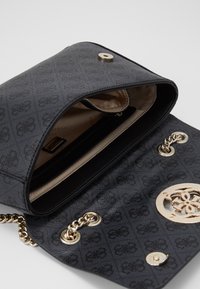 Černá texturovaná kabelka se zlatým logem, řetízkovými detaily a zapínáním na knoflík. Vnitřek má krémovou podšívku a samostatnou kapsu na zip.