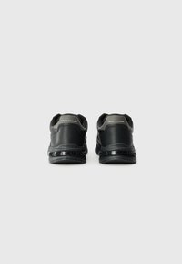 Chaussures de sport noires avec une tige en cuir texturé, col rembourré et semelle extérieure marquée. Forme arrondie avec un design minimaliste.