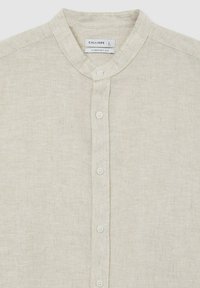 Camicia di lino beige con colletto alla coreana, presenta cinque bottoni bianchi sulla parte anteriore. Etichetta chiara che mostra la taglia L e "Comfort Fit."